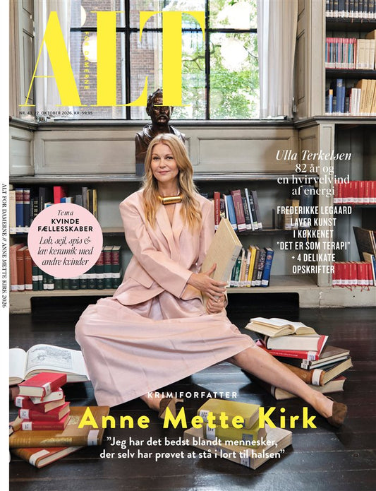 Forside af ALT for damerne nr. 43, 2026 med Anne Mette Kirk i lyserødt tøj, siddende blandt bøger på et bibliotek.