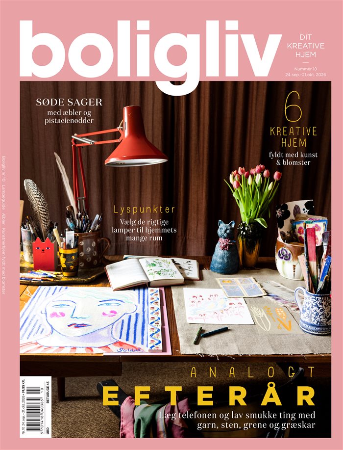 Forside af Boligliv nr. 10 med lyserød masthead og et kreativt arbejdsbord med tegninger, bøger, en rød lampe og blomster.