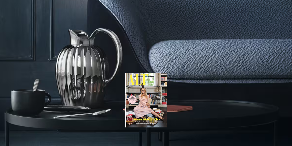 ALT for damerne og en Bernadotte-kande fra Georg Jensen på et mørkt sofabord foran en blå sofa.