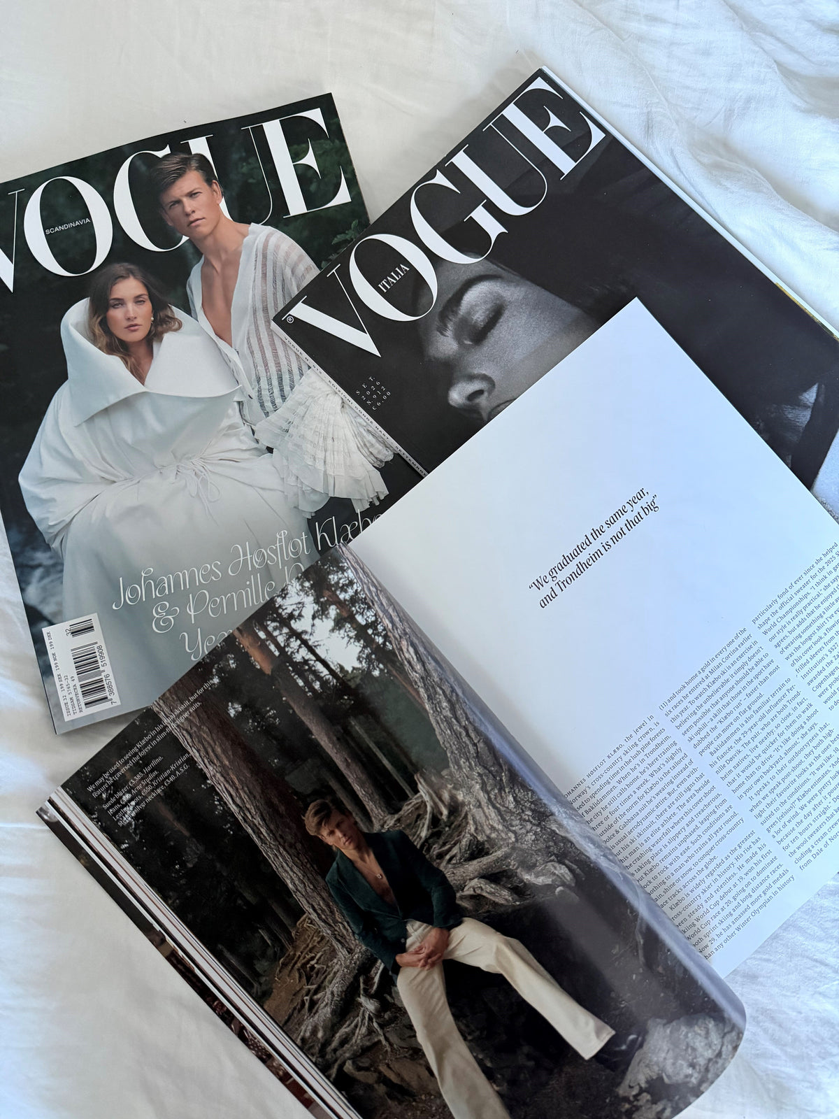 Vogue Scandinavia og Vogue Italia sammen med et åbent magasin på lyst sengetøj.