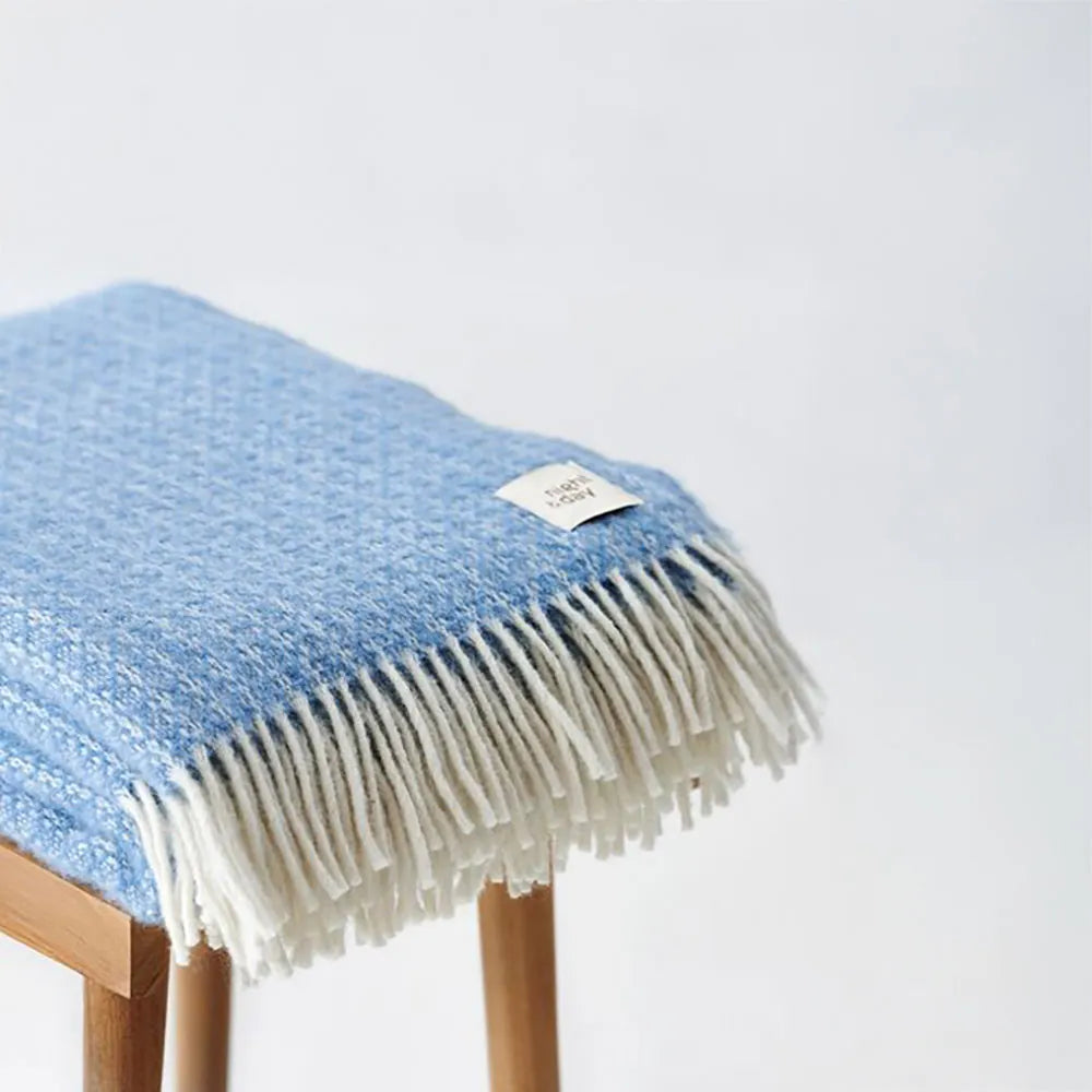 Lyseblå uldplaid fra Night & Day over en træskammel med hvid baggrund – WOOLMARK-certificeret 100% uld