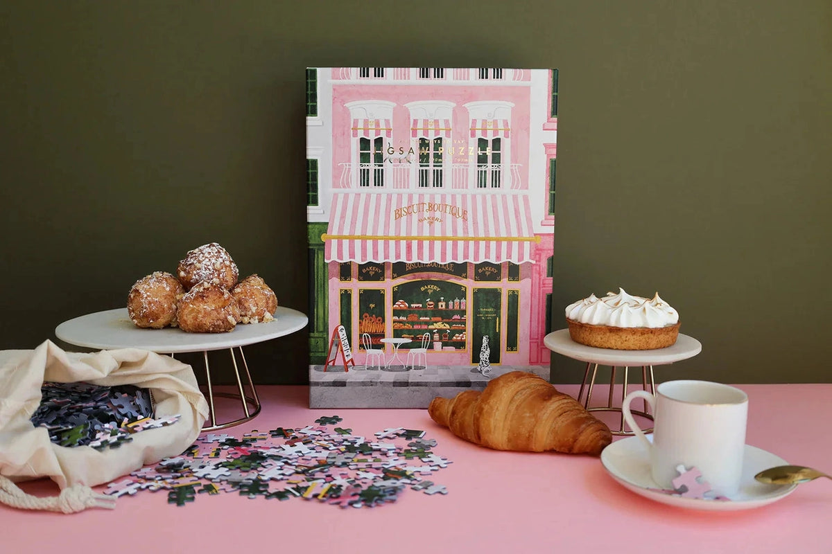 Pink Bakery-puslespil med æske og løse brikker på et rosa bord med kager, croissant og kaffekop