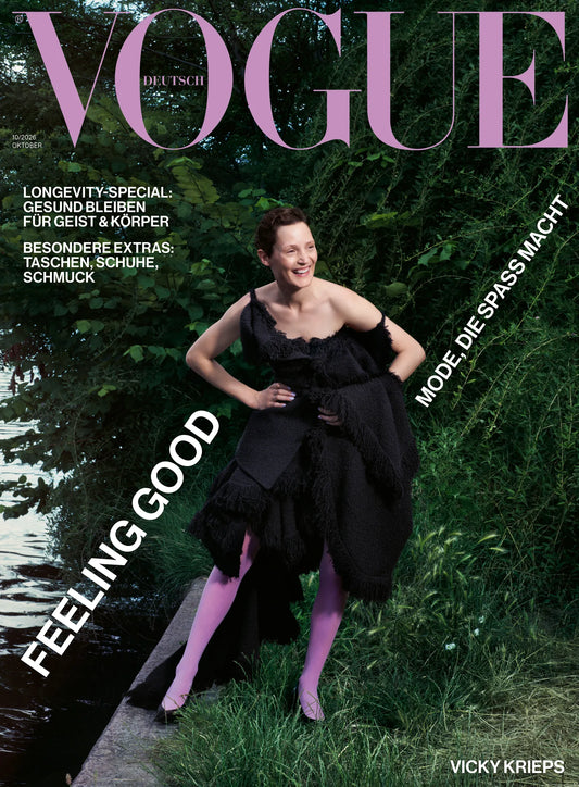 Forsiden af Vogue Germany oktober 2026 med en kvinde i sort kjole og lilla strømpebukser ved vandet, omgivet af grønne træer.