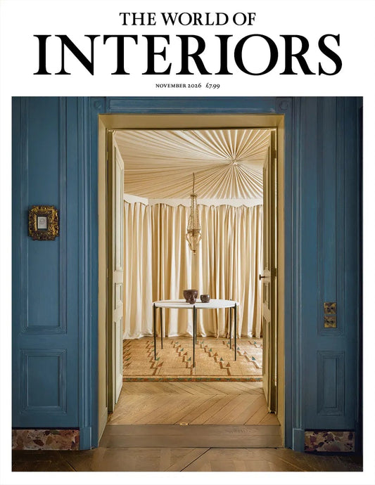 The World of Interiors november 2026 med blå vægge og en døråbning til et lyst rum med draperet loft, gardiner og et lille bord.